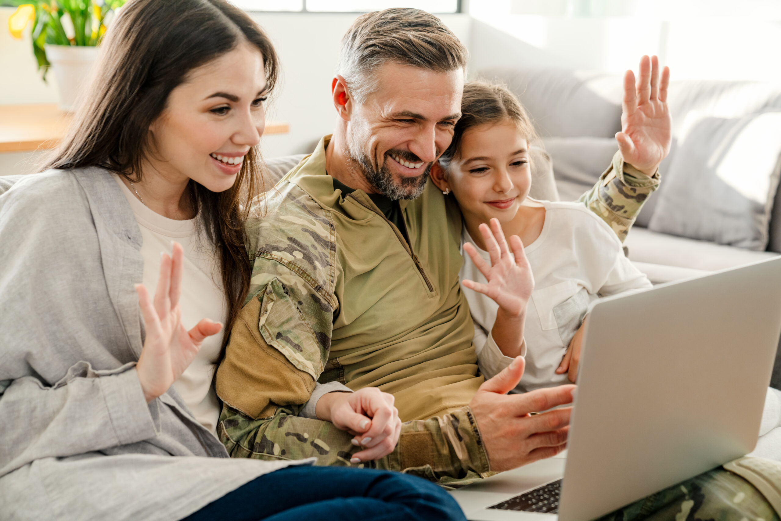 Happy military man waving hand with his family while using laptop